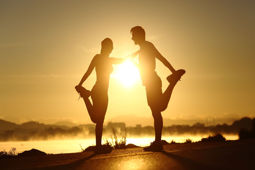 Couple supporting each other while stretching their hamstrings after a run (not a yoga pose)